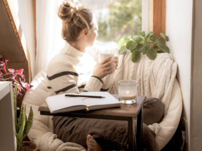 A cozy mental health break with an open journal, pen and coffee cup.Young Woman taking a mental health break to write in her journal stares out the window with coffee in hand